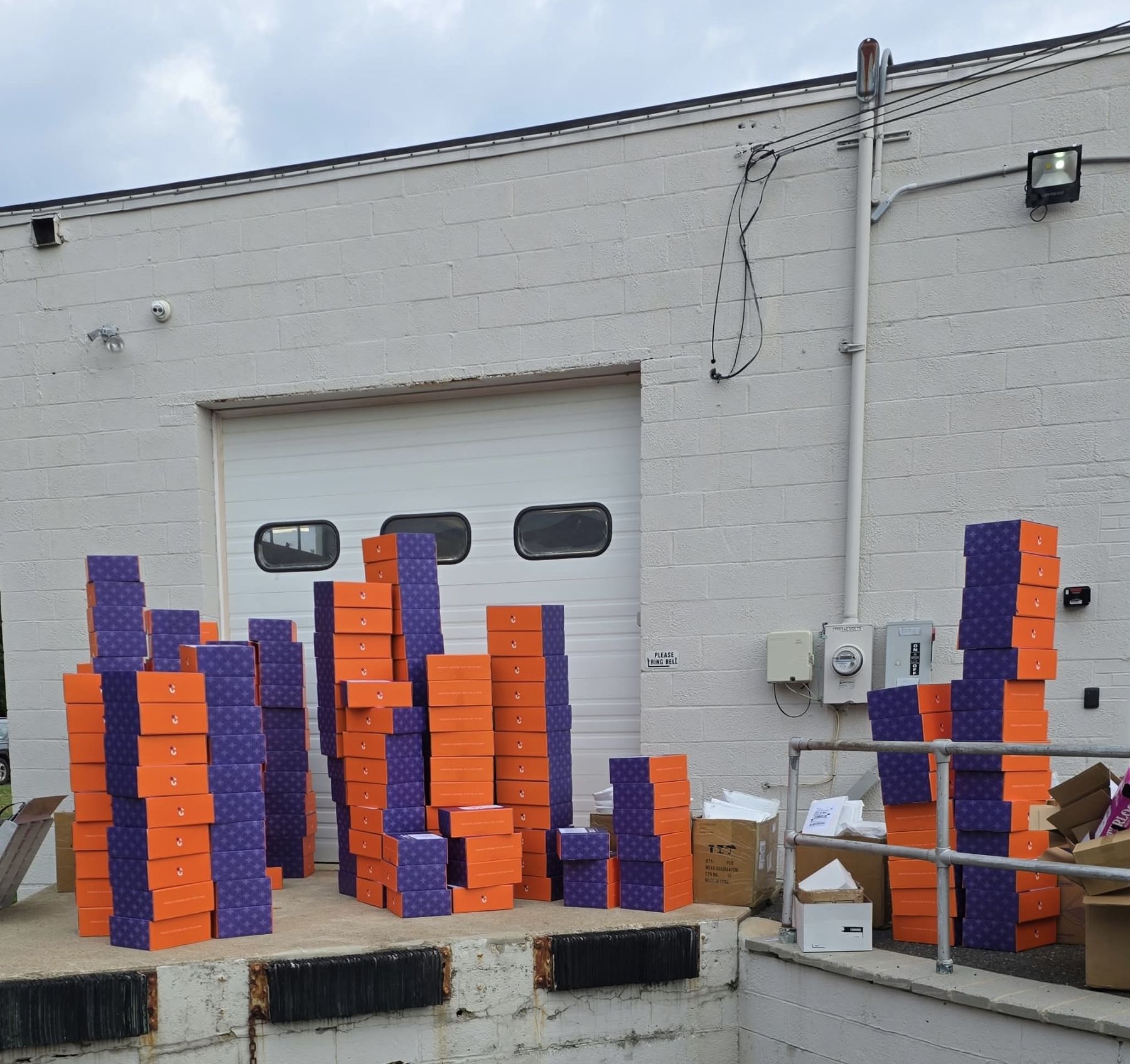 Hundreds of plum and orange Coulmed care-package boxes stacked on a loading dock, ready to ship